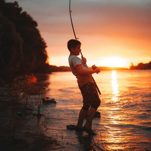 fisherman casting line into lake during sunset fishing trip