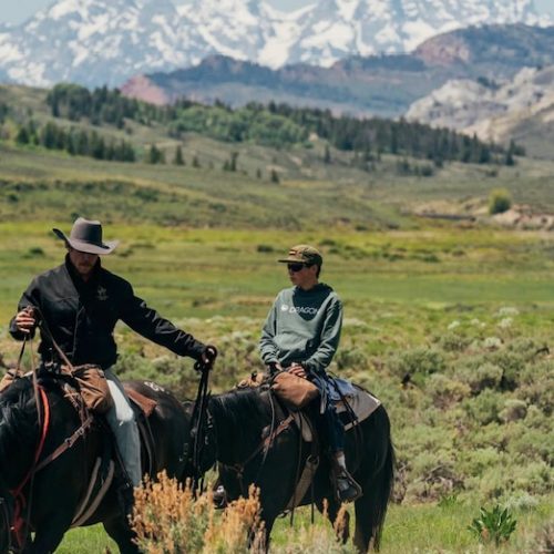 cowboys riding horses across scenic valley landscape