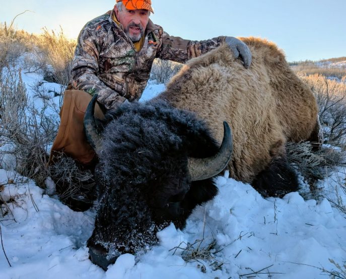 hunter posing with harvested bison during winter hunting trip