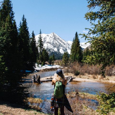 hiker walking along river surrounded by pine forest