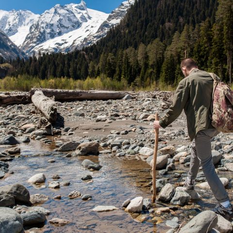 hiker crossing rocky mountain creek during wilderness adventure